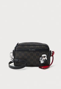 Melna krustu somiņa ar Karl Lagerfeld logo rakstu, sudraba detaļām, teksturētu materiālu un multfilmu varoņu akcentiem. Reguluojams siksniņas garums.