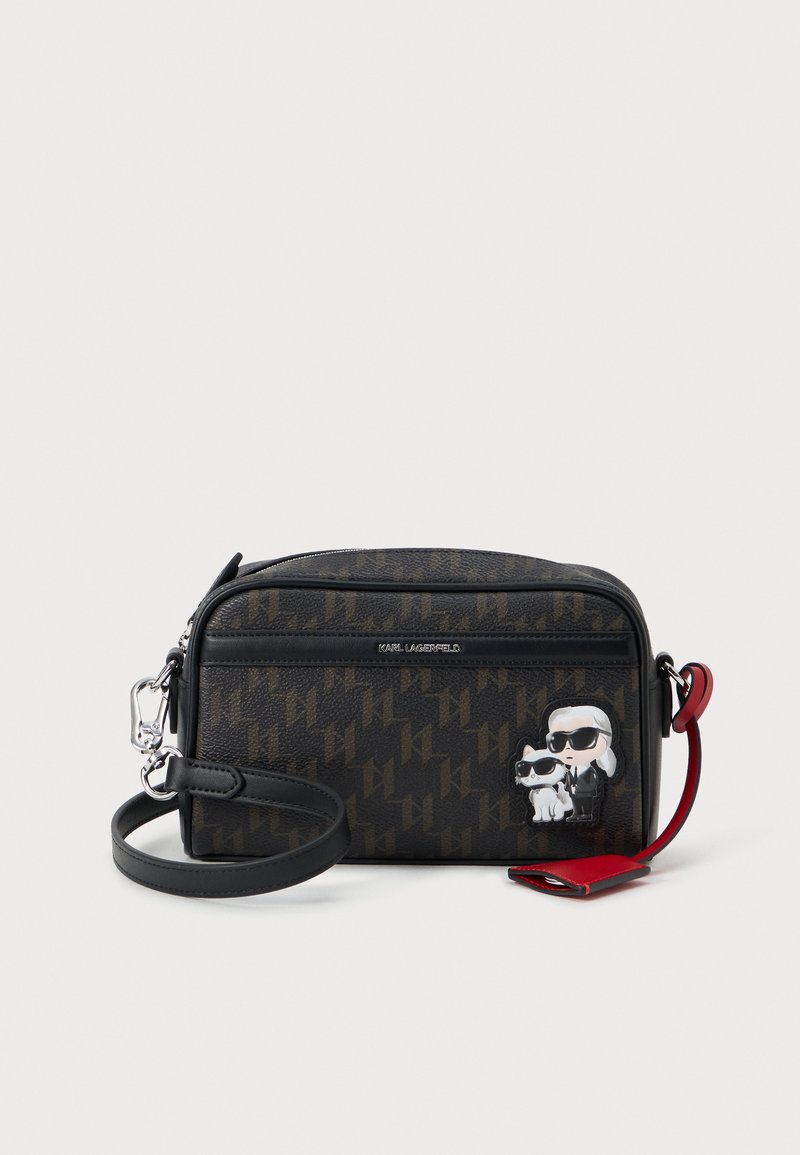 Melna krustu somiņa ar Karl Lagerfeld logo rakstu, sudraba detaļām, teksturētu materiālu un multfilmu varoņu akcentiem. Reguluojams siksniņas garums.