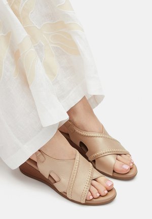 Beżowe skórzane sandały z krzyżującymi się paskami, ozdobione plecionymi akcentami i wycięciami. Miękki, teksturowany materiał oraz niski, układany obcas.