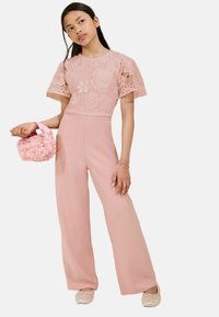 Combinaison rose avec un corsage en dentelle florale, un pantalon à jambes larges et des manches courtes. Accompagnée d'un petit sac à main floral rose.