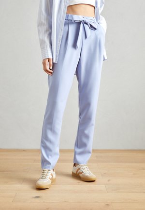 Un pantalon bleu clair taille haute avec une ceinture à nouer, en tissu lisse, doté de poches latérales et d'une coupe décontractée, associé à des baskets beiges.