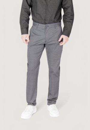 Pantaloni grigi a fantasia con vestibilità slim, dotati di chiusura a bottone e passanti per cintura, abbinati a scarpe da ginnastica bianche e una camicia nera.