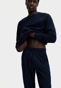 Marineblauer Pullover mit geripptem Muster, rundem Ausschnitt und langen Ärmeln. Kombiniert mit passenden Sweatpants mit Kordelzug, beide aus weichem Stoff.