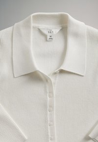 Witte geribbelde gebreide top met kraag en knoopsluiting aan de voorkant, middelgrootte, met label "The Set", gemaakt in Bangladesh.