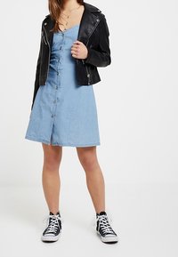 Denim A-linje klänning med framknappar, tillsammans med en svart lädermotojacka och svarta och vita hög-top sneakers.