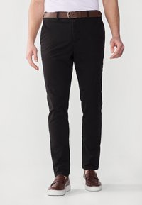 Svarta chinos i bomull med en mjuk textur, slim-fit design, tillsammans med ett brunt läderbälte och bruna slipskor.