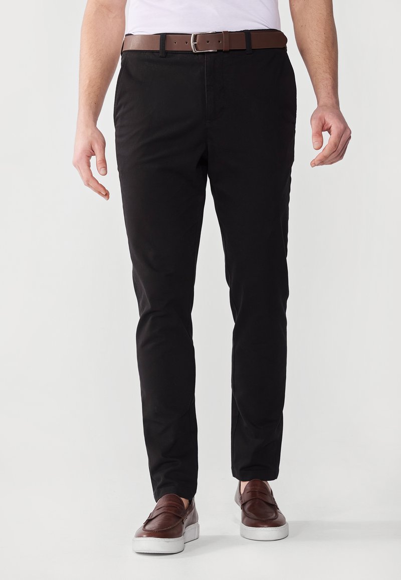 Svarta chinos i bomull med en mjuk textur, slim-fit design, tillsammans med ett brunt läderbälte och bruna slipskor.