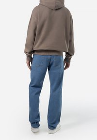 Hoodie i brunt tyg kombinerad med lösa blå jeans. Jeansen har bakfickor och diskreta sömmar. Vita skor fullbordar looken.