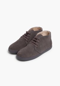 Bottines en daim gris à bout rond, avec des lacets sombres contrastants, des œillets dorés et une semelle en caoutchouc texturée. Doublure intérieure lisse.