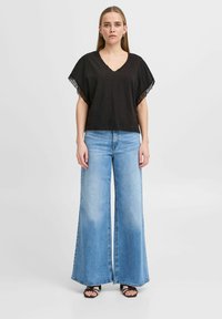 Zwarte V-hals top met brede mouwen, gecombineerd met lichtblauwe, wijde denim jeans. De jeans hebben een vervaagde wassing en een zoomlijn op de enkels.