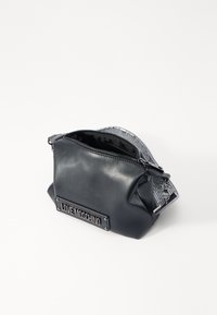 Black faux leather bag with a textured silver mesh top, featuring a prominent logo plate and a zip closure. Compact and rounded design.