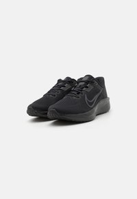 Baskets de sport noires avec une tige en mesh, bout rond, semelle flexible et lacets plats. Caractéristiques d'un logo discret et d'accents texturés sur les côtés.