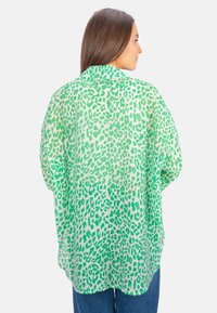 Green leopard print blouse with a loose, draped silhouette. Lightweight, sheer material, long sleeves, and a soft, smooth texture.