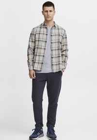 Camicia di flanella a quadri beige e navy, indossata sopra una maglietta grigia. Abbinata a pantaloni jogger scuri e scarpe sportive navy.