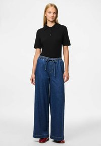 Melnas īsām piedurknēm polo krekls ar apkakli, apvienots ar platajām tumši zilām džinsu biksēm ar elastīgu jostu un auklu.