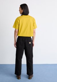 Camiseta de algodón amarilla de manga corta, combinada con pantalones negros holgados que cuentan con dos bolsillos traseros y un pequeño parche de logo.