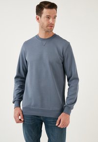 Felpa grigia in cotone con maniche lunghe, scollo rotondo, polsini e orlo a coste; texture liscia, con dettagli di cucitura minimi.