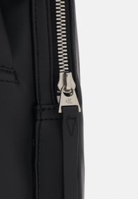 Borsa in pelle nera vista laterale con una cerniera argentata dotata di una linguetta con il marchio e cuciture a contrasto. Texture liscia con un design elegante.