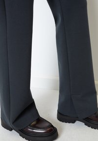 Mørkegrå joggebukser laget av mykt stoff, med en avslappet passform og sideslits, paret med kraftige brune loafers.