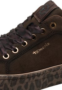 Close-up of brown suede sneaker with leopard print platform sole, satin dark patterned laces, gold eyelets, and "tamaris" logo in gold lettering.
