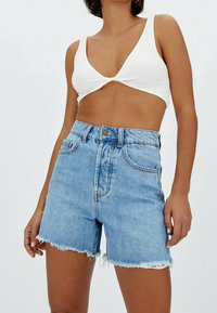Denimshorts i ljusblått med hög midja, trasig fåll och klassisk femfickdesign. Matchas med en vit ribbad crop top.