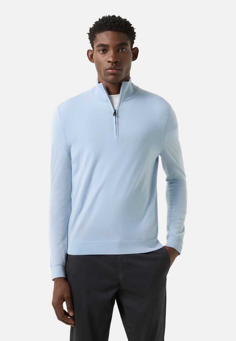 Lichtblauwe trui met rits, gemaakt van een zachte, gestructureerde brei. Voorzien van een hoge kraag en geribbelde manchetten. Gecombineerd met een donkere broek.