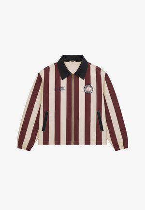 Woman wearing burgundy and beige striped jacket, light gray shorts, white socks, and silver sneakers, standing against a plain gray background.