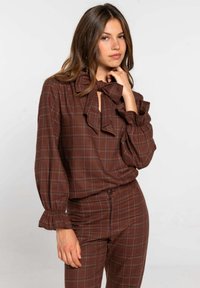Blusa de cuadros marrón con cuello y mangas con volantes, combinada con pantalones a juego de cuadros. Textura suave, con detalle de botones en los pantalones.