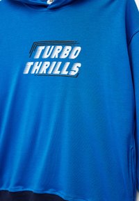 Niebieska bluza z kapturem z napisem "TURBO THRILLS" w białym i czarnym. Gładki materiał, luźny krój, z przednią kieszenią i sznurkiem w kapturze.