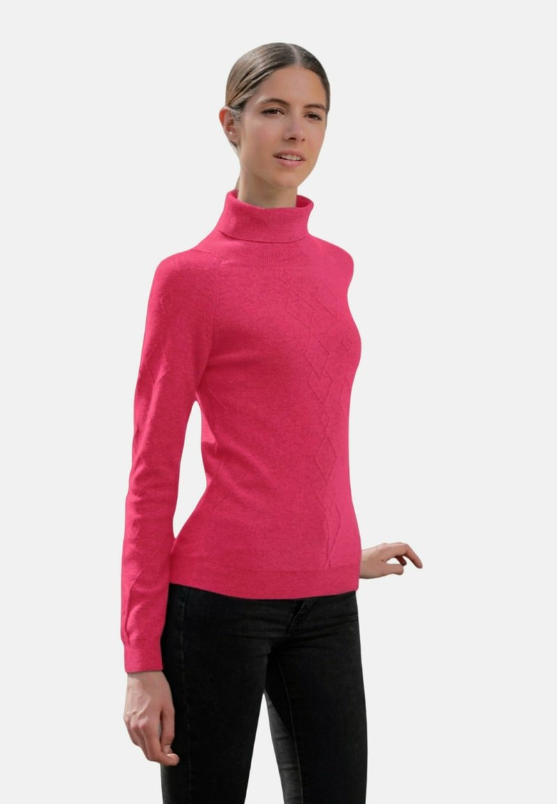 Pull à col roulé rose ajusté en tissu doux ; présente un motif en losange subtil sur le devant ; assorti à un pantalon noir.