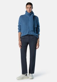 Pullover in lana blu a maglia cable con sciarpa abbinata, abbinato a pantaloni navy a taglio dritto con cuciture laterali a contrasto e sneakers bianche.