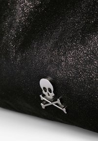 Hopeinen pääkallo ja ristiluut -symboli tekstuurilla varustetulla mustalla pinnalla, jossa on hienovarainen glitterefekti, kuvattuna lähikuvassa.