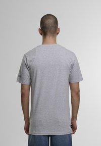 Grå bomulds T-shirt med korte �ærmer og rund halsudskæring, med et mærke på venstre ærme. Glat tekstur, afslappet pasform.