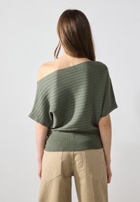 Pull-over olive crop sans épaule avec texture côtelée et manches courtes, associé à un pantalon large beige taille haute avec poches arrière.