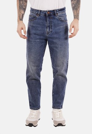 Jeans de denim azul con un corte relajado, diseño de cinco bolsillos y cierre de botón. Llevados con zapatillas blancas, que presentan sutiles detalles de desgaste.