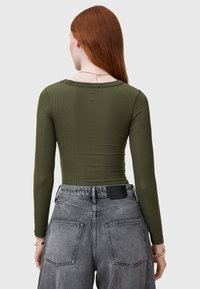 Maglietta a maniche lunghe, verde oliva a coste con scollo rotondo, abbinata a jeans in denim grigi sbiaditi a vita alta con tasche posteriori.