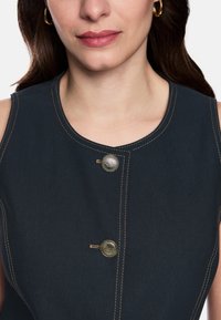 Marineblaues ärmelloses Kleid mit rundem Ausschnitt, das kontrastierende goldene Nähte und eine dekorative Metallknopfdetail vorne aufweist.