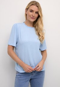 Top azzurro chiaro a maniche corte con un motivo texturizzato, scollatura rotonda a balze e vestibilità morbida; abbinato a jeans azzurro chiaro.
