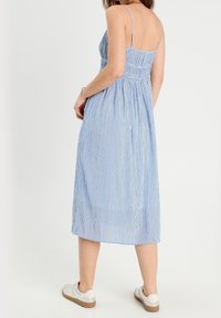 Robe midi rayée bleu et blanc avec un corsage smocké et de fines bretelles spaghetti, associée à des baskets blanches.