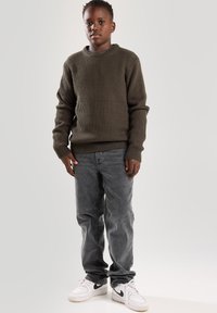 Olivenfarbener gerippter Pullover mit Rundhalsausschnitt, kombiniert mit ausgebleichten grauen Jeans und weißen Sneakers. Strukturierter Stoff, lässige Passform und entspannter Stil.