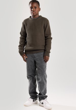 Maglione a coste olive con scollatura rotonda, abbinato a jeans grigi sbiaditi e sneakers bianche. Tessuto testurizzato, vestibilità rilassata e stile casual.