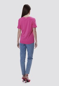 Pink cotton t-shirt med korte ærmer, rund halsudskæring og en lille detalje nær kraven, kombineret med blå stribede jeans og pink højhælede sko.