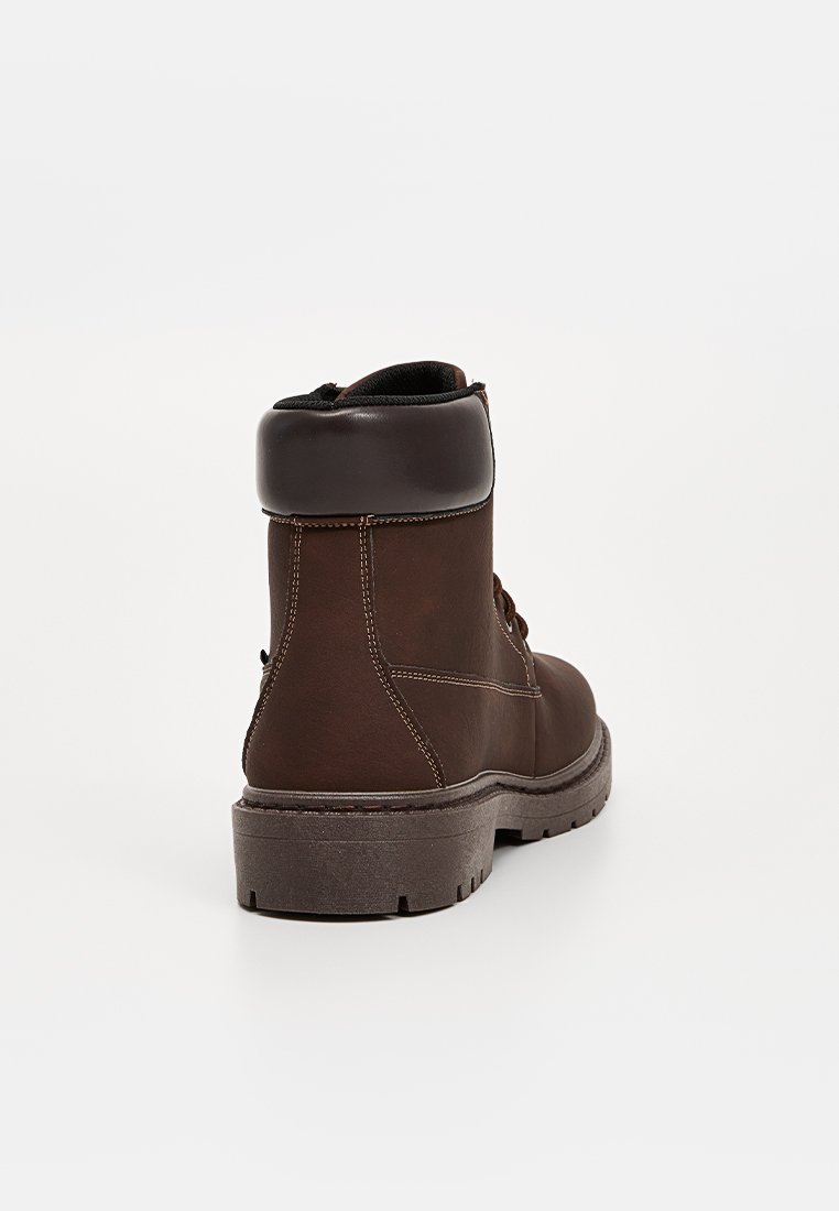 Stivale alla caviglia in pelle marrone con punta rotonda, risvolto imbottito e suola in gomma testurizzata. Presenta cuciture beige e chiusura con lacci.