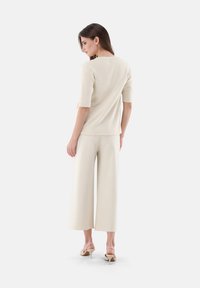 Beige Strickoberteil mit ellenbogenlangen Ärmeln, kombiniert mit weit geschnittenen cremfarbenen Hosen und nude-farbenen Slingback-High Heels, die eine schlichte, moderne Silhouette präsentieren.