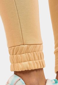 Dunne perzikkleurige legging met een geribbelde enkelboord. Gladde textuur, getailleerd ontwerp en gestikte naden. Close-up zicht op de enkel.