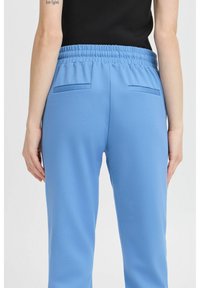 Pantalones de chándal azul claro con cintura elástica, dos bolsillos traseros y una textura suave, mostrados desde la vista trasera.