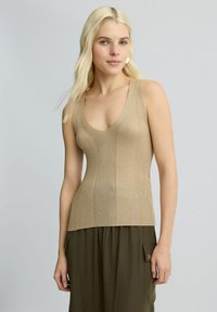 Top in raso beige a costine con scollatura a V, design aderente e spalline larghe. Abbinato a pantaloni larghi verde oliva.