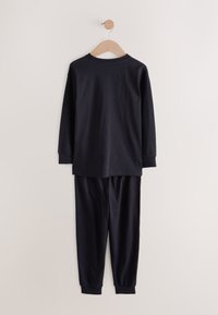 Zwarte pyjama met lange mouwen en bijpassende broek, hangend aan een houten hanger tegen een lichte, effen muur.