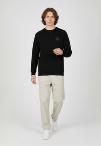 Czarna bluza z okrągłym dekoltem i rękawami raglanowymi, zestawiona z jasnobeżowymi spodniami i białymi trampkami. Prosty i schludny design.