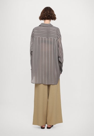 Camicia leggera e trasparente a righe grigie con una vestibilità comoda, abbinata a pantaloni larghi beige. Maniche lunghe, dettagli con bottoni ai polsini.
